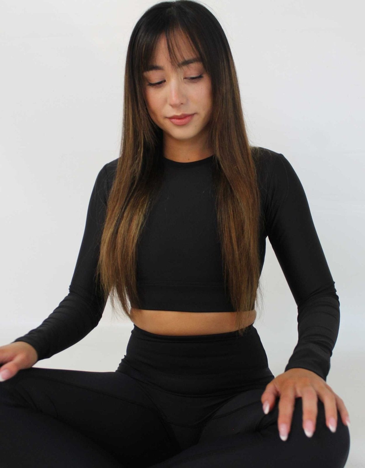 Girl sitting with legs crossed and hands on her knees. She is looking down. Wearing long sleeve black activewear top and leggings from Vocus Vit. Vocus vit is a sustainable women's activewear brand that uses recycled materials and ethical manufacturing. Based in Northern Ireland. Shipping worldwide.Sizes XS (8) TO XXL (18).