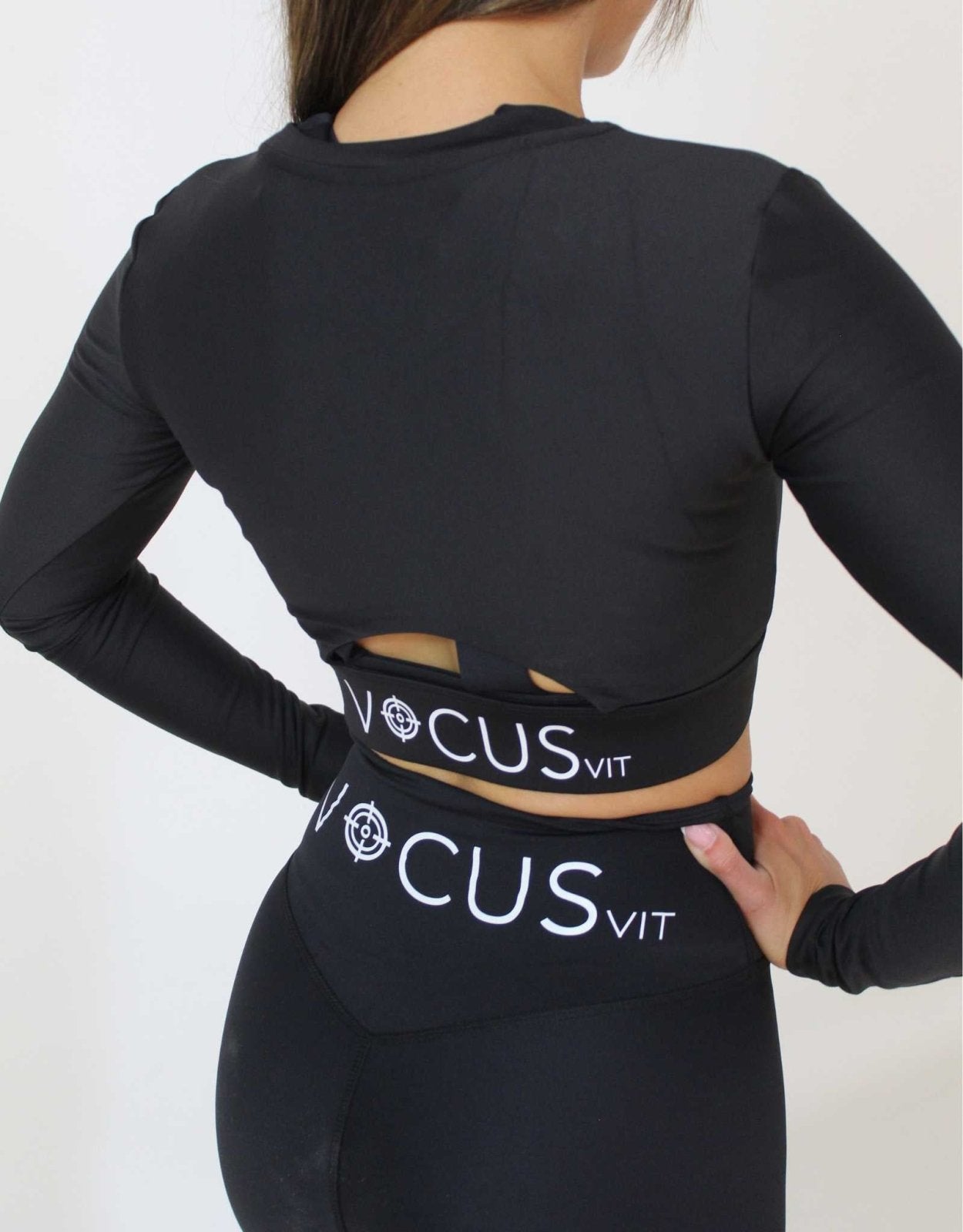 girl standing with hands on her waist wearing Vocus Vit black long sleeve top and leggings. Large white logo on the back of activewear. Vocus vit is a sustainable women's activewear brand that uses recycled materials and ethical manufacturing. Based in Northern Ireland. Shipping worldwide.Sizes XS (8) TO XXL (18).