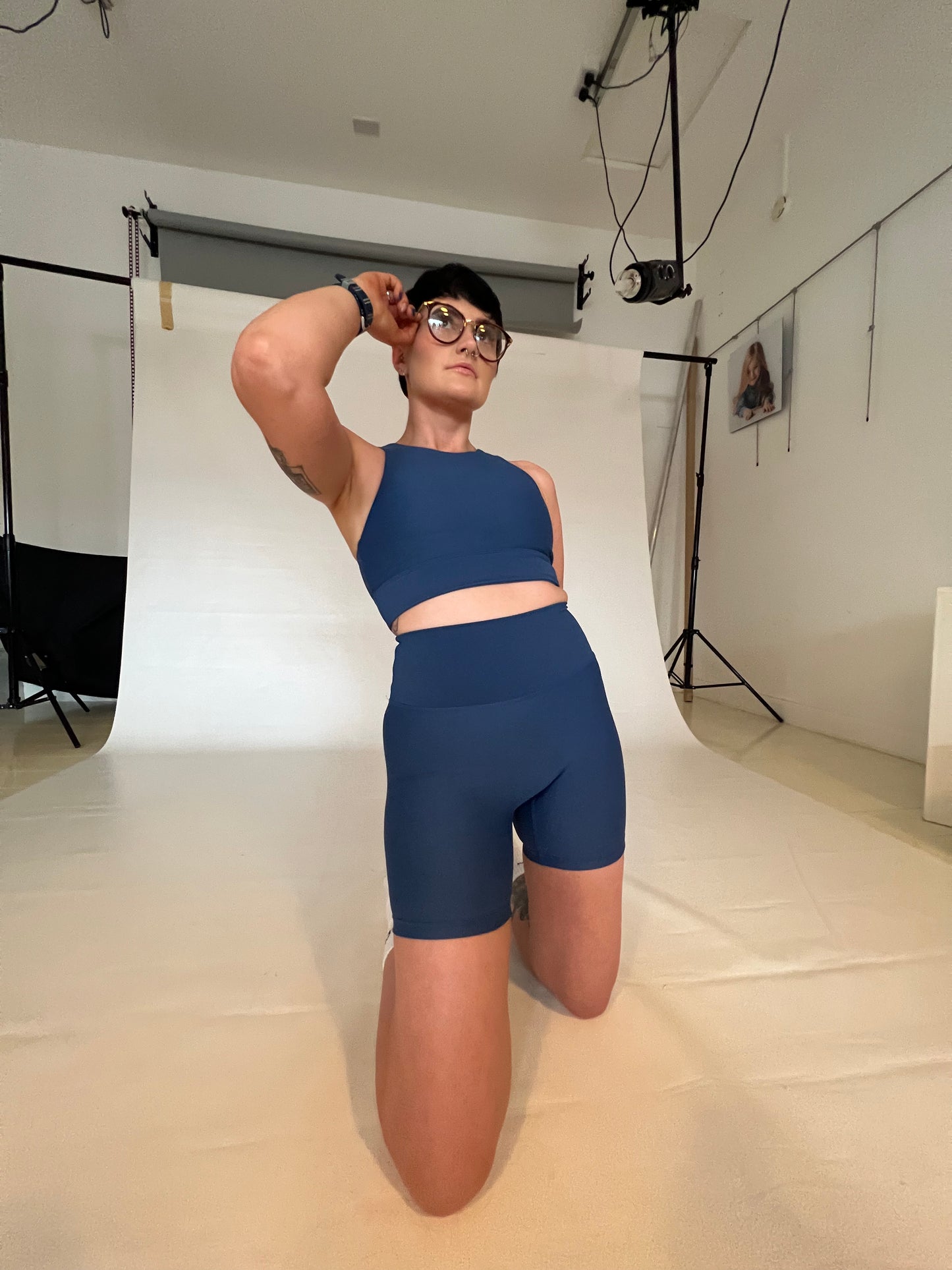 Girl wearing glasses and Vocus Vit sports bra and shorts in blue. She is posing on her knees and leaning backwards. Vocus vit is a sustainable women's activewear brand that uses recycled materials and ethical manufacturing. Based in Northern Ireland. Shipping worldwide.Sizes XS (8) TO XXL (18).