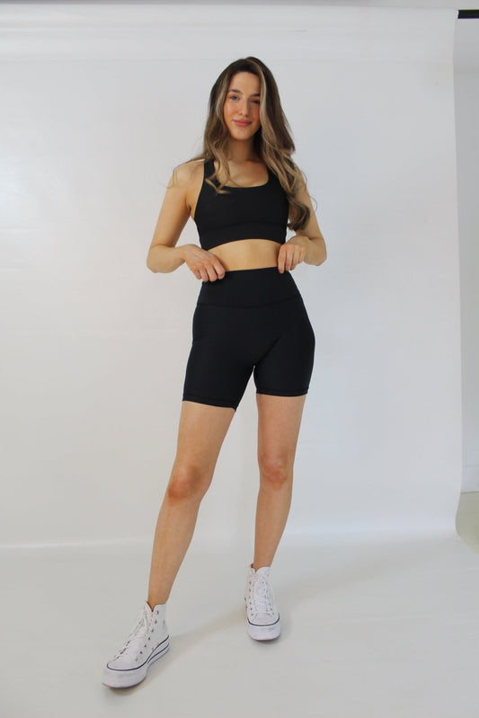 Model standing wearing black Vocus Vit legacy shorts and sports bra. Vocus vit is a sustainable women's activewear brand that uses recycled materials and ethical manufacturing. Based in Northern Ireland. Shipping worldwide.Sizes XS (8) TO XXL (18).