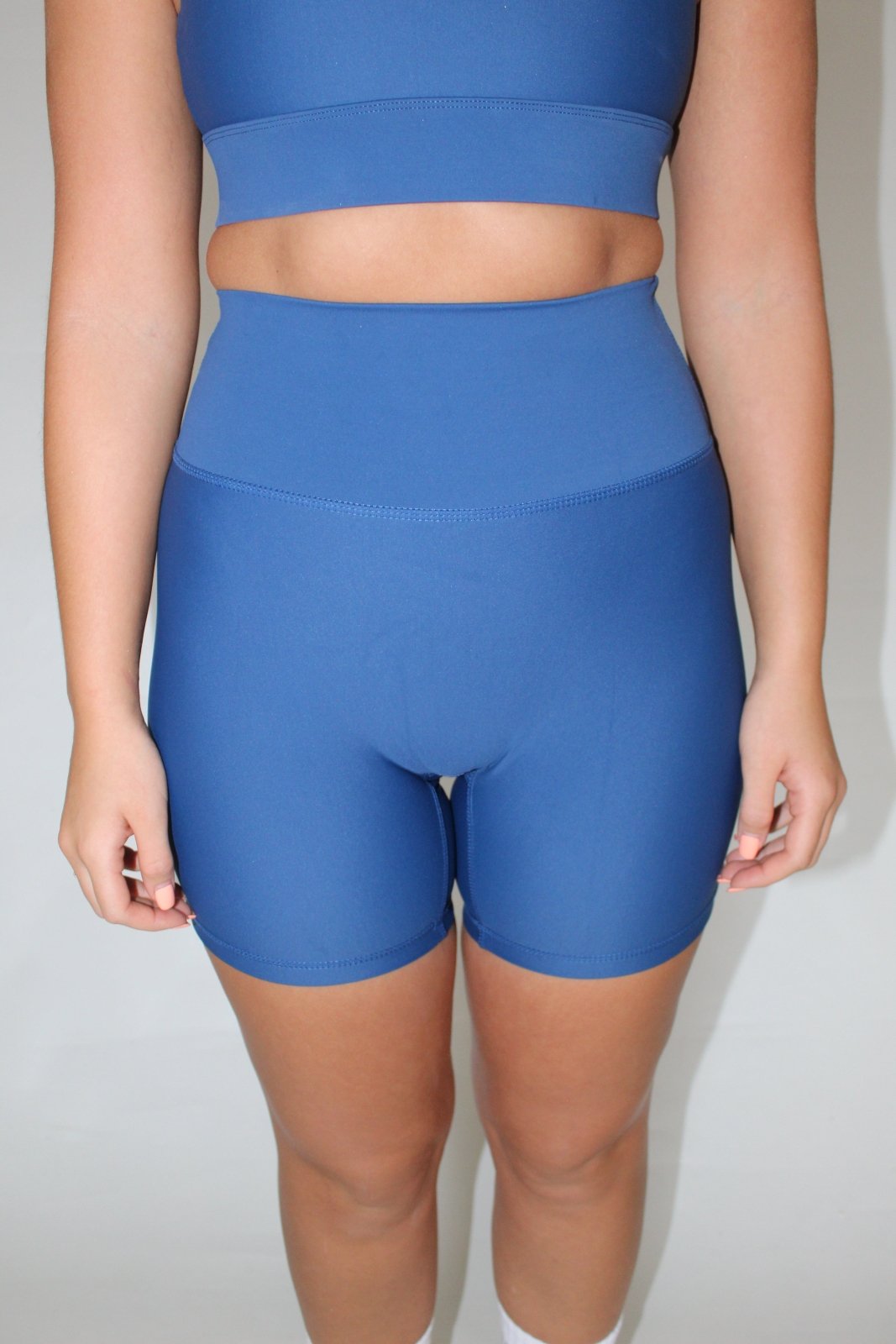 Girl wearing blue Vocus Vit shorts with hands by her side. Photo cut off from waist down. Vocus vit is a sustainable women's activewear brand that uses recycled materials and ethical manufacturing. Based in Northern Ireland. Shipping worldwide.Sizes XS (8) TO XXL (18).