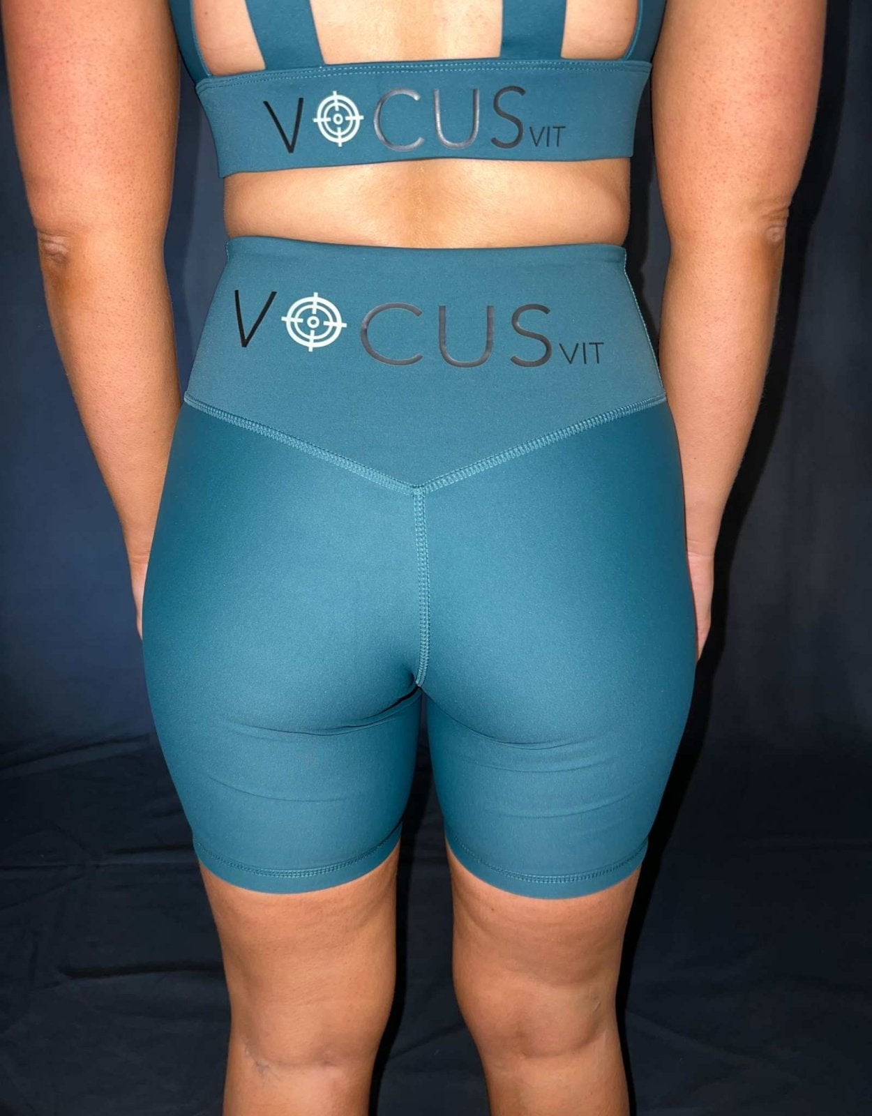 Girl from waist down. Wearing green (evergreen) Vocus Vit shorts. Close up photo of shorts. Vocus vit is a sustainable women's activewear brand that uses recycled materials and ethical manufacturing. Based in Northern Ireland. Shipping worldwide.Sizes XS (8) TO XXL (18).