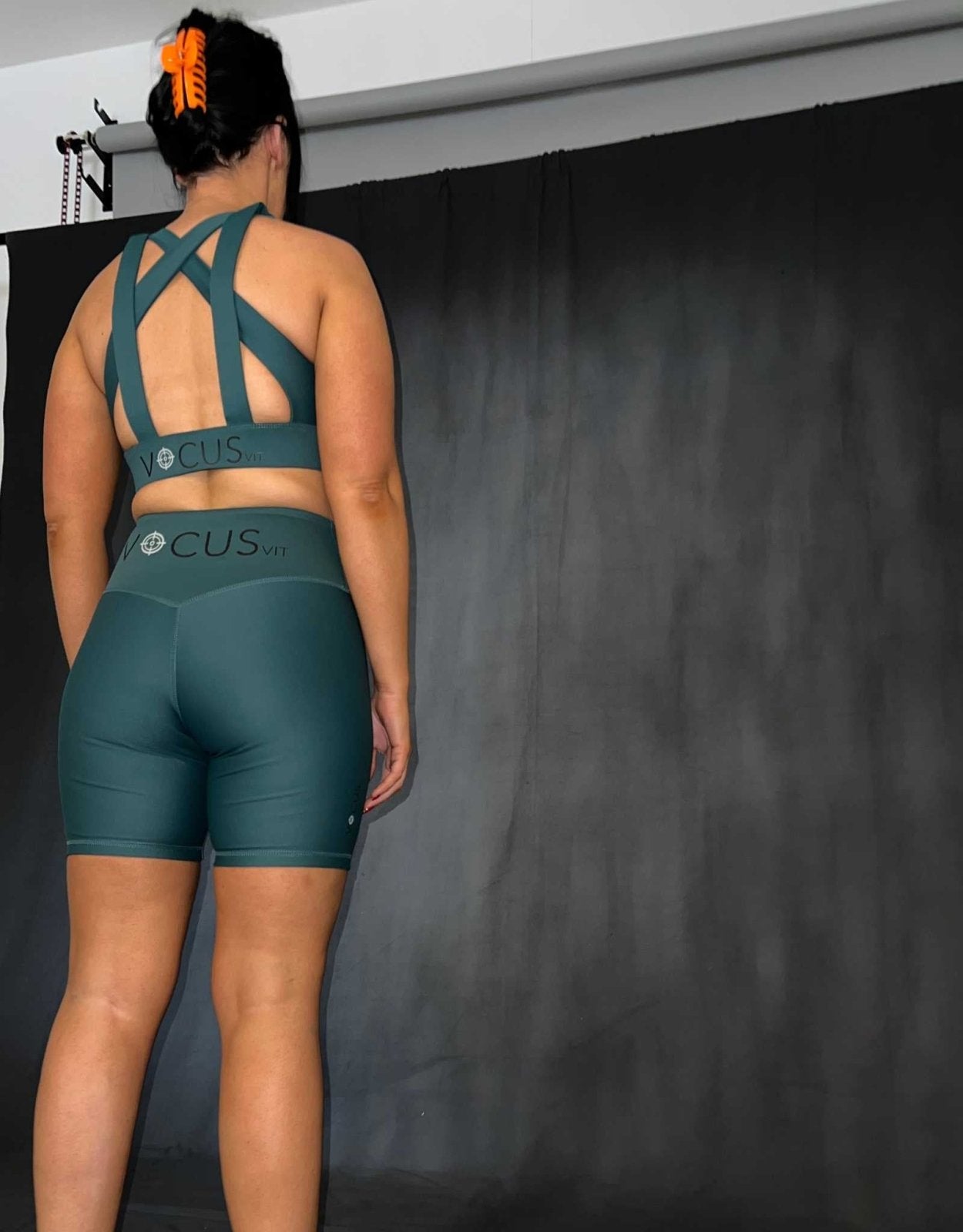 girl standing with her back to the camera. she has green activewear on. she is wearing a sports bra and shorts. Vocus vit is a sustainable women's activewear brand that uses recycled materials and ethical manufacturing. Based in Northern Ireland. Shipping worldwide.Sizes XS (8) TO XXL (18).