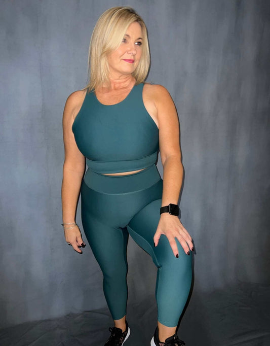 Women standing wearing green (evergreen) activewear from vocus vit. she has a sports bra and 7/8 leggings on. Vocus vit is a sustainable women's activewear brand that uses recycled materials and ethical manufacturing. Based in Northern Ireland. Shipping worldwide.Sizes XS (8) TO XXL (18).