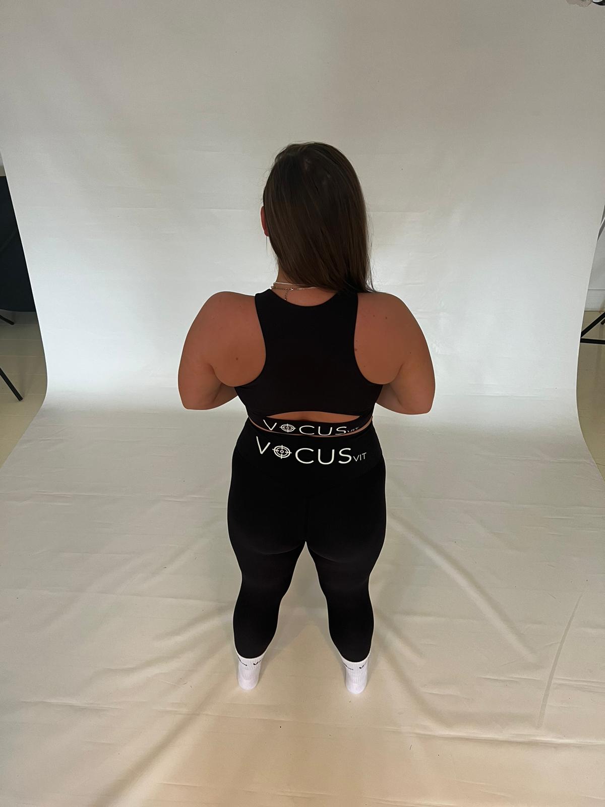 girl standing back to camera wearing black sports bra and leggings from vocus vit. Vocus vit is a sustainable women's activewear brand that uses recycled materials and ethical manufacturing. Based in Northern Ireland. Shipping worldwide.Sizes XS (8) TO XXL (18).