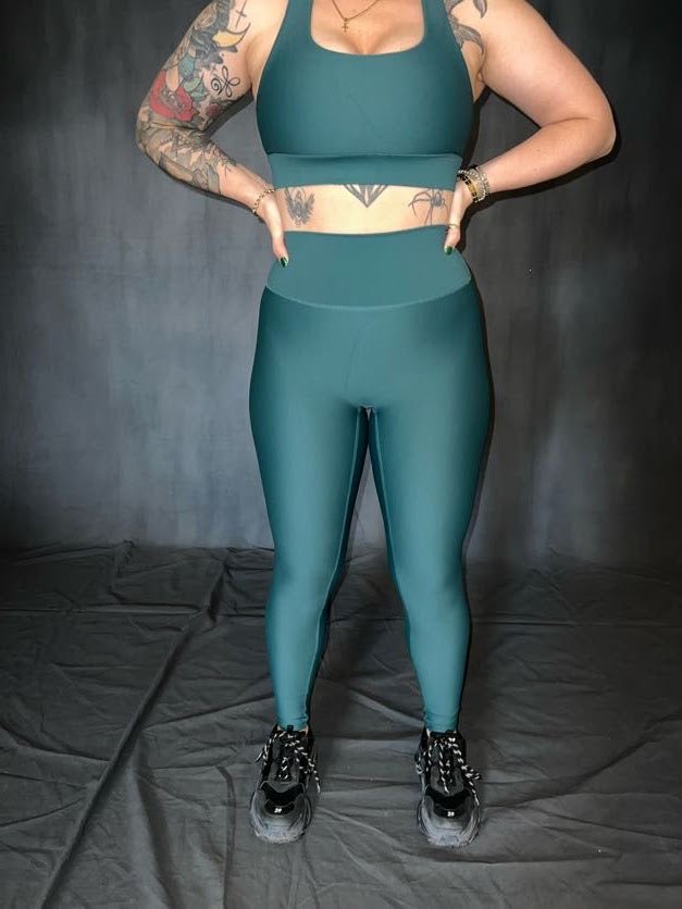 girl standing with hands on waist and tattoos on her stomach and arm. she is wearing green (evergreen) full length leggings from vocus vit. 